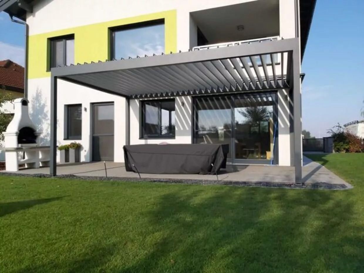 Modernes Haus mit überdachter Terrasse, umgeben von Grünflächen und einem einladenden Außenbereich.